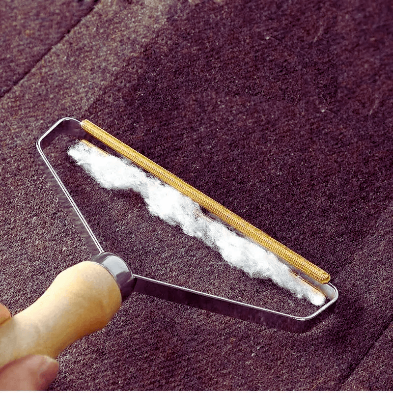 Portable pet hair and lint remover brush in use on dark fabric, showcasing effective removal of hair and lint with a wooden handle.