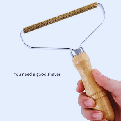 Hand holding a wooden manual pet hair and lint remover brush with metal edge for cleaning clothes and furniture.