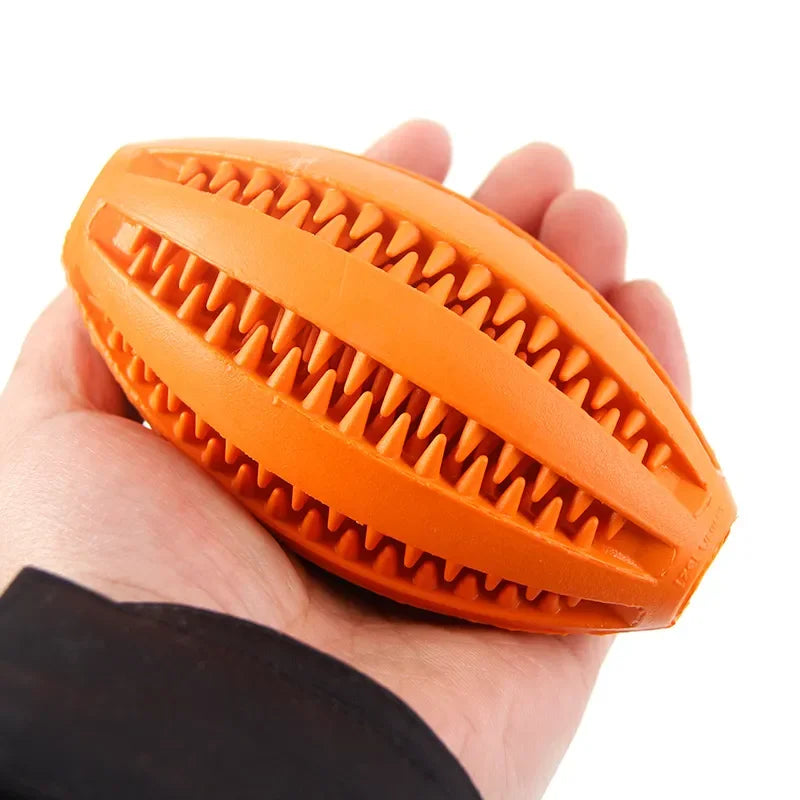 Orange natural rubber dog chew ball with teeth-cleaning ridges, held in hand, ideal for fetch and teething.