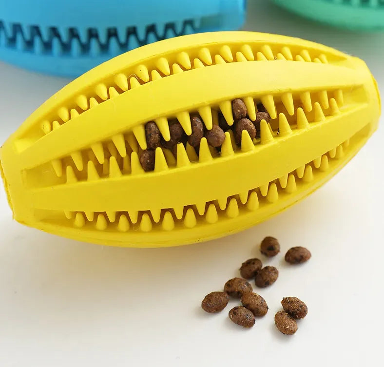 Yellow natural rubber chew ball for dogs with treat slots, ideal for teething and fetch games, shown with treats nearby.